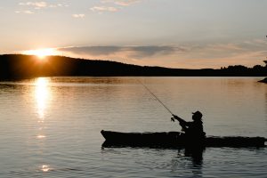 Man fishing on his small boat at sunset in the middle of a lake.