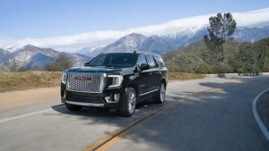 Black 2021 GMC Yukon Denali model driving down a mountain road with mountains in the background.